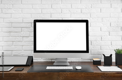 Modern computer with blank screen on table near brick wall. Space for design