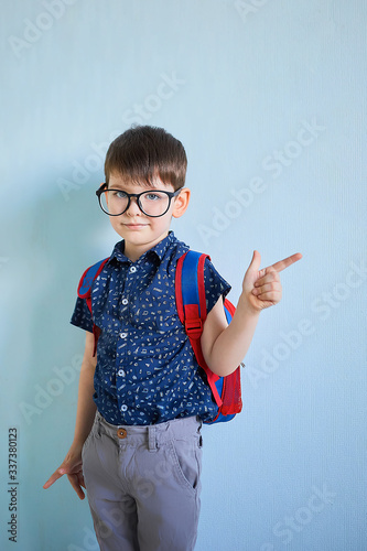 a cute European boy with glasses points his finger at an empty background . blank for design and advertising on blue background