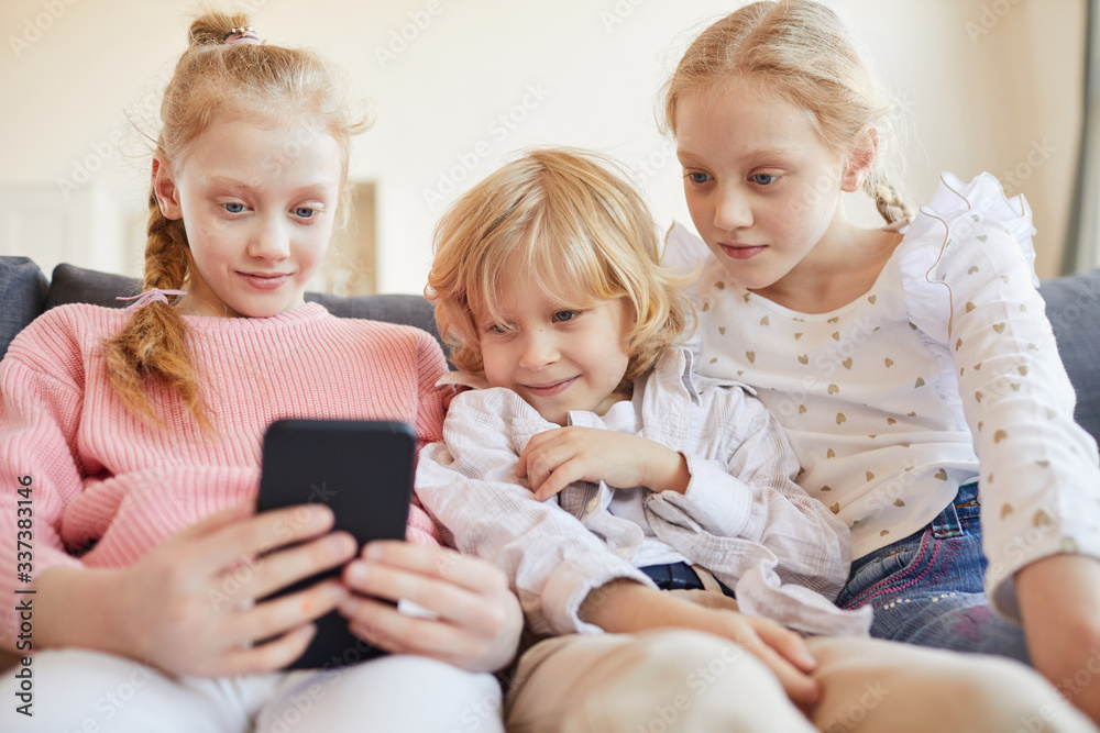 Group of friends sitting on sofa and playing in online games on mobile phone at home Group of friends sitting on sofa and playing in online games on mobile phone at home