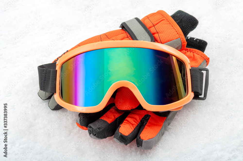 Snowboarding and skiing protective gear and winter extreme sports concept with ski goggles and cold weather gloves isolated on white snow background