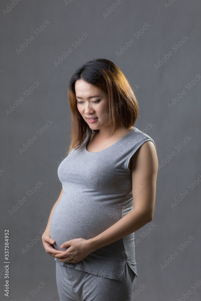 Pregnant woman in gray dress hold hands on belly in white background. Pregnant woman in gray dress hold hands on belly in white background.