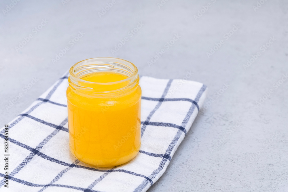 Homemade clarified butter in a glass jar on neutral background with space for text Homemade clarified butter in a glass jar on neutral background with space for text