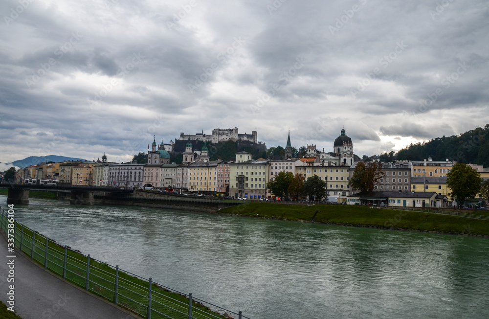 Autumn view with Salzach river, Salzburg Cathedral (Salzburger Dom) and Hohensalzburg Fortress on hill top with cloudy sky at the background.