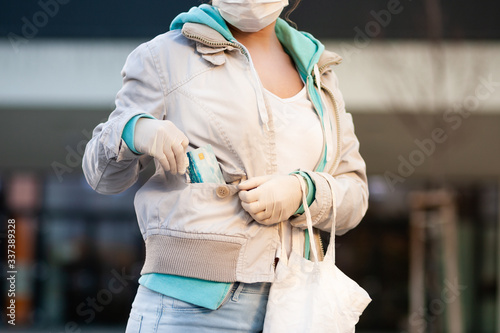 Woman holding a credit card and wearing latex gloves and disposable medical mask before shopping in front of a supermarket. Paying with credit card is more safer than cash.
