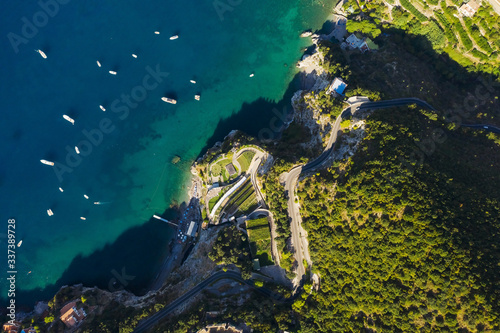Aerial shot to the sea with boats and rocky green shore. Serpentine road along the mountains. South Italy. Beaautiful landscape. View from above. © Artem