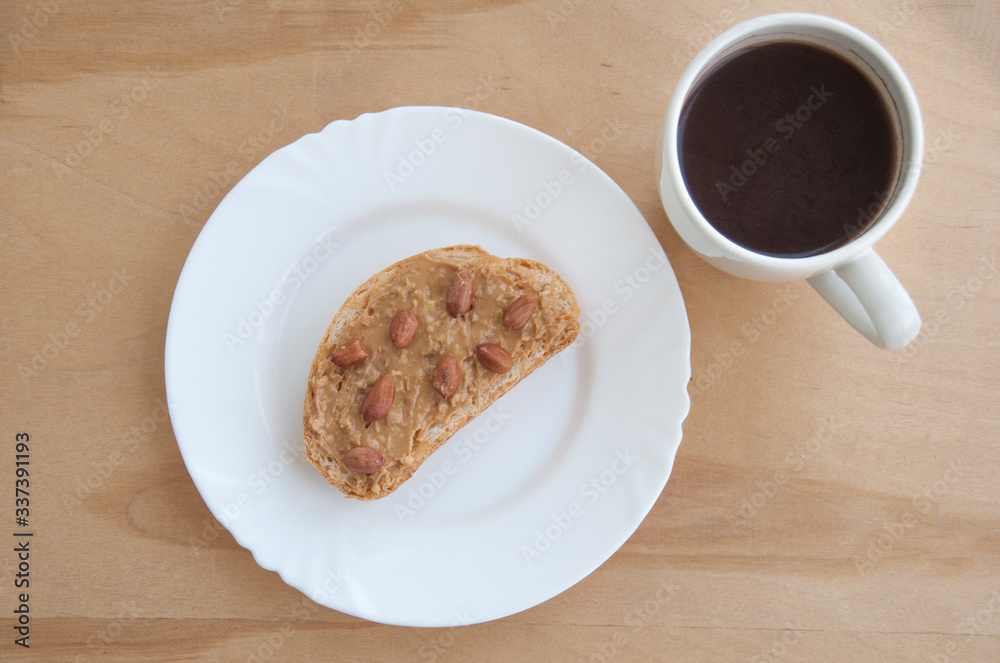A plate with toasted bread and peanut butter and a cup of coffee on the wooden table. Top view A plate with toasted bread and peanut butter and a cup of coffee on the wooden table. Top view