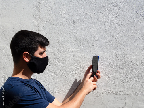 Young man with a black face mask using a mobile