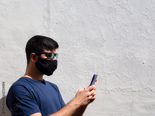 Young man with a black face mask using a mobile with glasses