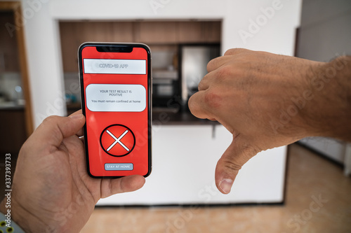 A person doing a thumbs down holding a smartphone that swhows a coronavirus app developed by the Government that tells you the COVID 19 test results and give a message of 