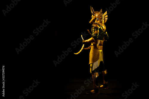 a male actor in a suit of an Egyptian mythology character, the golden deity Jackal Anubis, twists buugeng in yellow light on a black background photo