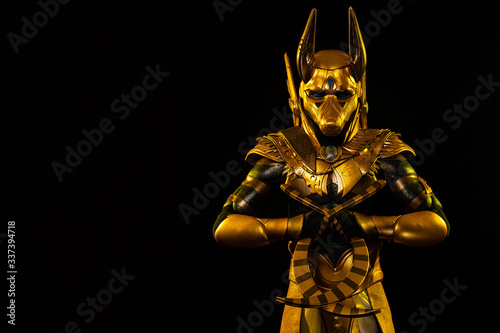 a male actor in a suit of an Egyptian mythology character, the golden deity Jackal Anubis, twists buugeng in yellow light on a black background photo