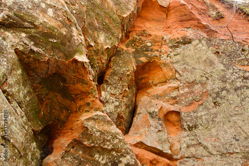 Red sandstone cliff with uneven surface. Limestone rock with cracks and slots.