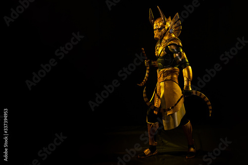 a male actor in a suit of an Egyptian mythology character, the golden deity Jackal Anubis, twists buugeng in yellow light on a black background