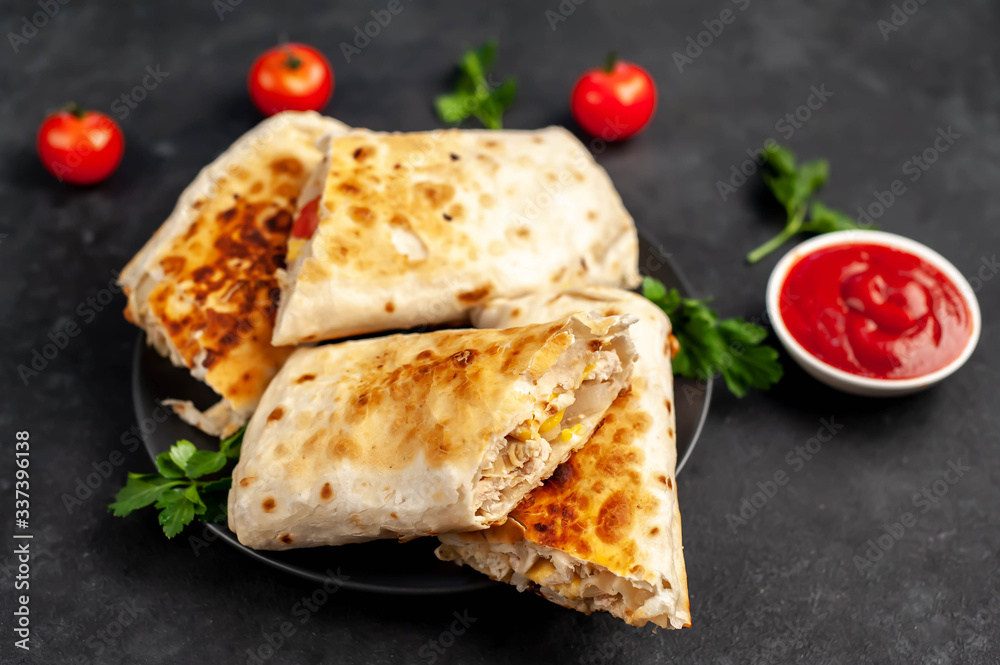 Burrito wraps with chicken and vegetables 
in a black plate , against a background of concrete , 
Mexican shawarma