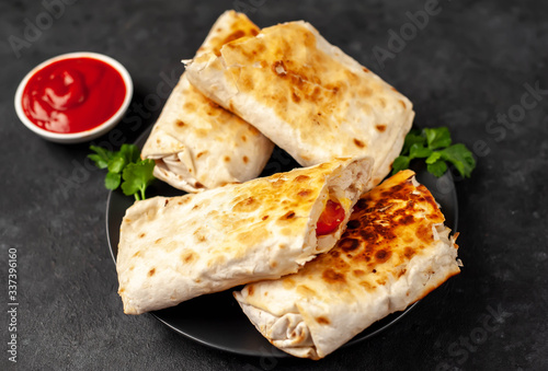 Burrito wraps with chicken and vegetables 
in a black plate , against a background of concrete , 
Mexican shawarma