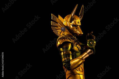 a male actor in a suit of an Egyptian mythology character, the golden deity Jackal Anubis, twists buugeng in yellow light on a black background