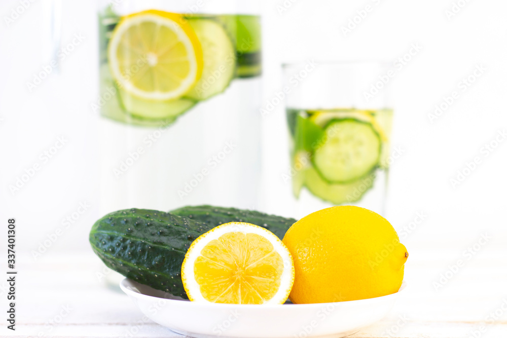 Health care, fitness, healthy eating concept. Fresh cool lemon cucumber drink with water, cocktail, detox drink, lemonade in a glass jug and a glass. cucumbers and lemon on a plate Health care, fitness, healthy eating concept. Fresh cool lemon cucumber drink with water, cocktail, detox drink, lemonade in a glass jug and a glass. cucumbers and lemon on a plate