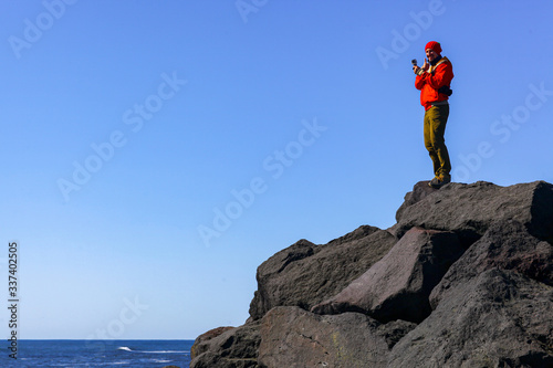 A man wearstands on the stone beach looking at rocks