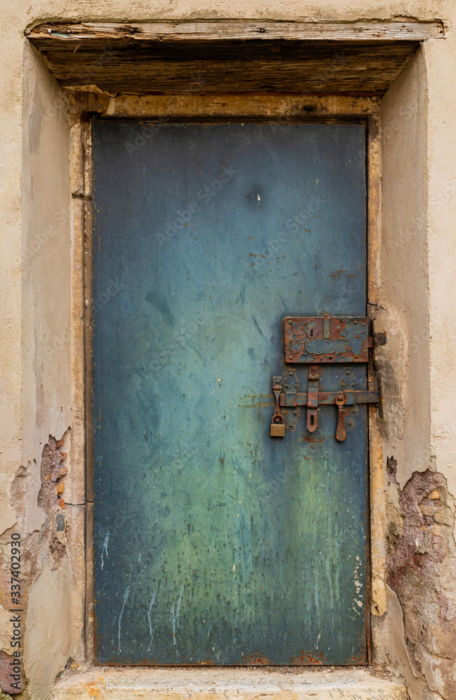 An old and mysterious green iron door, ancient and rusty bolt, signs of wear and tear, walls peeling from time, sun and rain. Renaissance park of Villa Celimontana in Rome. Celio hill. Italy.