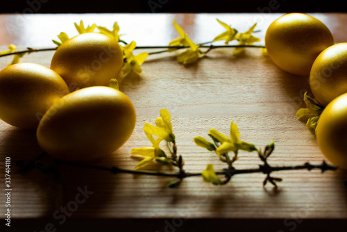 Golden color Easter eggs and yellow flowers on the wooden background. Side view. Easter 2020