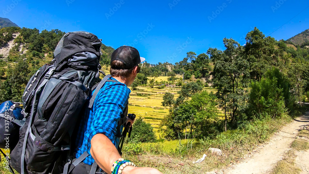 A man in hiking outfit taking a selfie while trekking along Annapurna Circuit in Nepal. He is enjoying the view and trek. There is a lush green Himalayan valley around him. Cheerful moments.