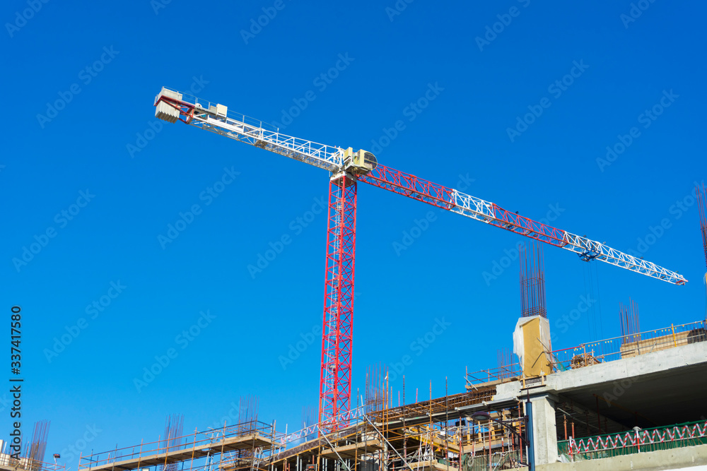 Single high-rise construction crane on the blue sky background. Building construction site with crane. Single high-rise construction crane on the blue sky background. Building construction site with crane.