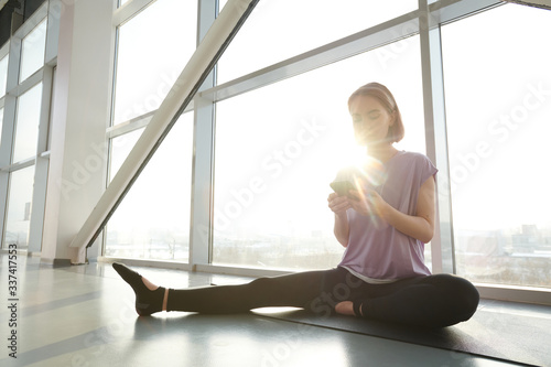 Young fit woman in activewear sitting on mat with one leg stretched