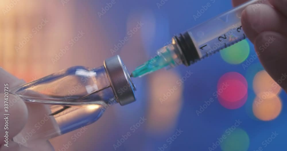 Injection with needle taking in transparent fluid. Vial filled with vaccine or other medicine. Close-up shot on laboratory background.
