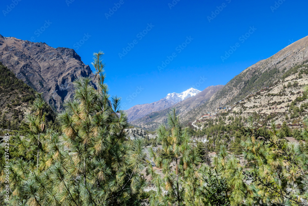 A Himalayan valley seen Annapurna Circuit Trek, Nepal. There is a small village on the side of the valley. In the back there are high snow caped mountains. Emptiness and serenity. A Himalayan valley seen Annapurna Circuit Trek, Nepal. There is a small village on the side of the valley. In the back there are high snow caped mountains. Emptiness and serenity.