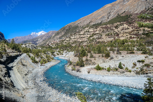 A panoramic view on river in Himalayan valley seen from Annapurna Circuit Trek, Nepal. Turquoise color of the river, big stones popping out of the river. Green forest around. Idyllic landscape.