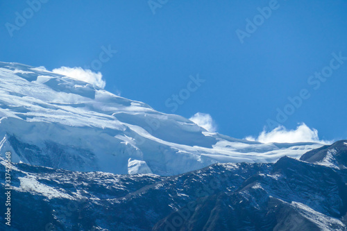 A close up view on snow caped Himalayan peak seen from Annapurna Circuit Trek, Nepal. Sharp and steep slopes of the mountain. Powder snow being blown by strong wind. First sunbeams reaching the peak © Chris