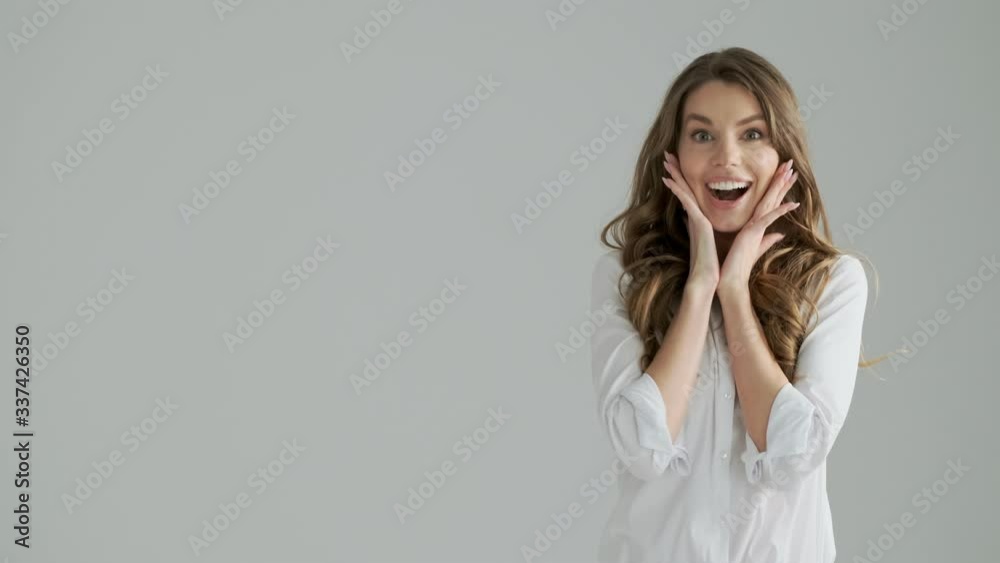 A happy woman is looking to the side and raised her hands while rejoicing isolated over a gray background in studio A happy woman is looking to the side and raised her hands while rejoicing isolated over a gray background in studio