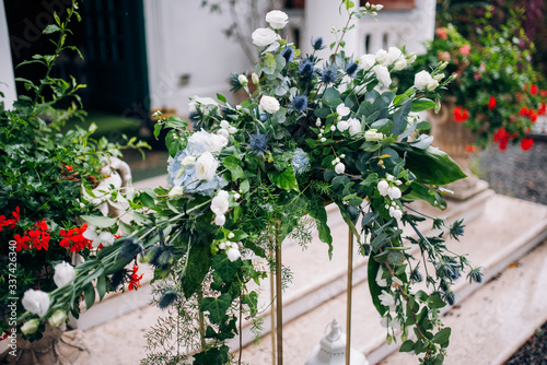 the arrangement of flowers at the wedding stands on a metal high stand  consists of many greens and white flowers