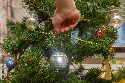 Hang a balloon on an artificial Christmas tree at home. Decorate the Christmas tree in the apartment.