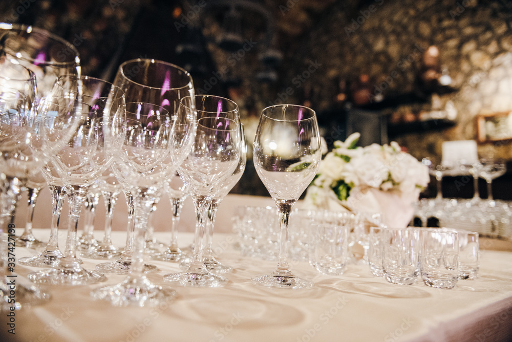 Empty wine glasses are standing on a table covere with tablecloth, there are white flowers on the background Empty wine glasses are standing on a table covere with tablecloth, there are white flowers on the background