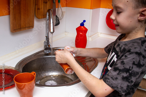 Wash dirty orange cups in the sink with a dishwashing sponge. Cleaning dishes after guests, family, Breakfast, dinner, lunch. The boy helps his beloved parents. Caring child.