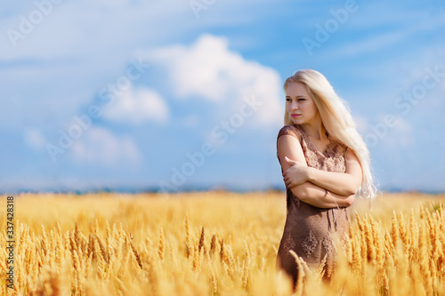 A girl with white and long hair walks in a field where wheat grows