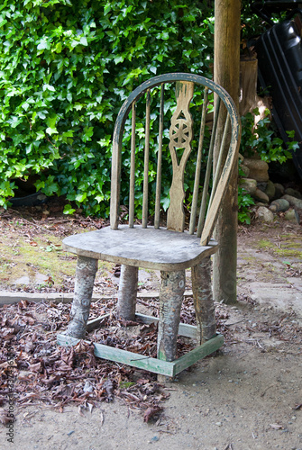 Rustic wood chair outdoors which legs have been made by tree branches.  Unique way a broken object has been recycled for use.