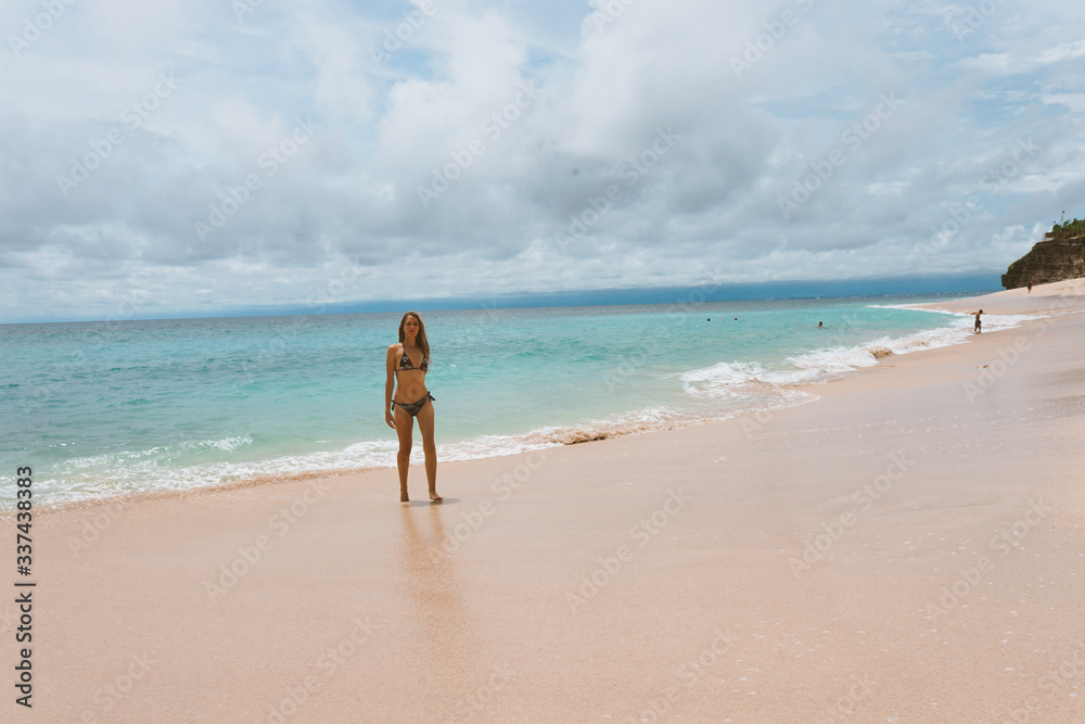 Beautiful and young girl in a swimsuit posing on the ocean and sea with blue waves. Woman in a swimsuit model and fashion posing. Relax and relaxation on the island of Bali Beautiful and young girl in a swimsuit posing on the ocean and sea with blue waves. Woman in a swimsuit model and fashion posing. Relax and relaxation on the island of Bali