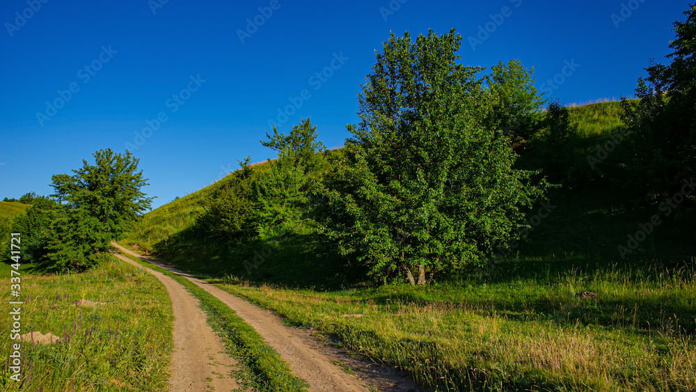 Dirt road at the foot of a hill, panoramic rural landscape.