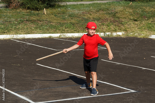 an eight year old plump boy in a red t shirt and cap throws a wooden bat on the asphalt