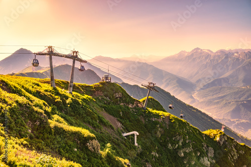 Vew in the summer sunset to the ski resort Rosa Khutor from the top of the Aibga range. The cable car is illuminated by the pink and orange sunset. Beautiful orange sunset in mountains
