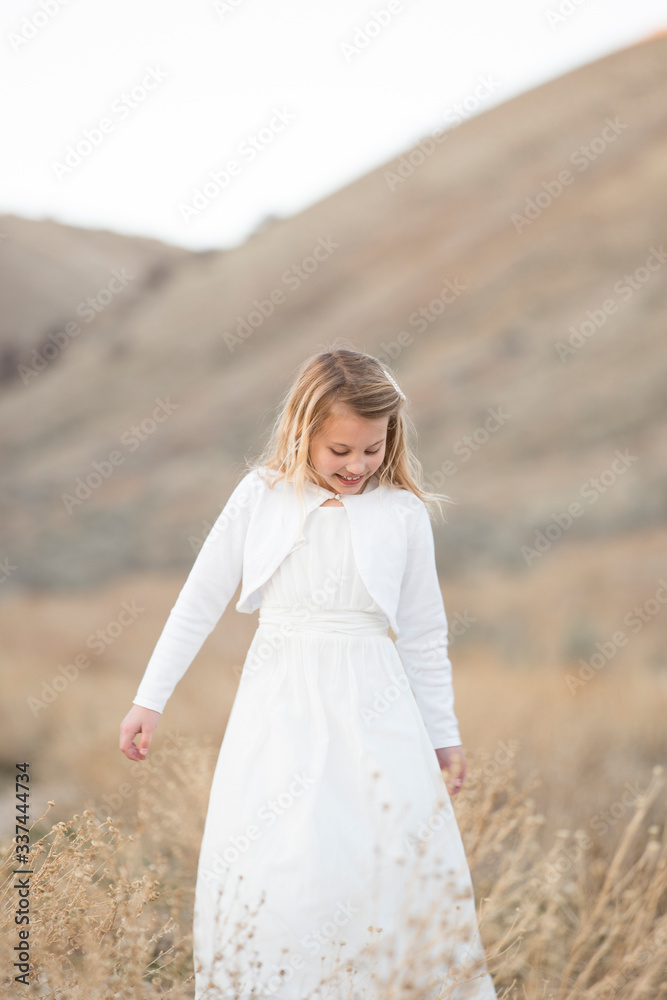 A little girl in a white dress outside among the dry grass and foothills A little girl in a white dress outside among the dry grass and foothills