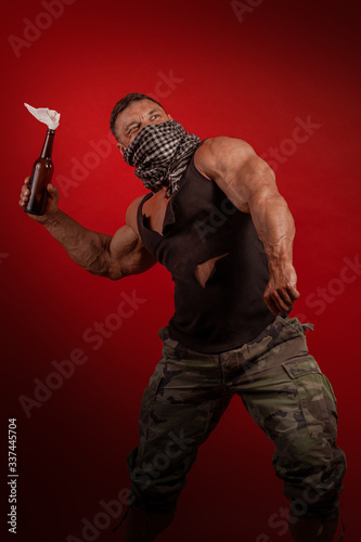 Young male athlete protester with a closed face with a Molotov cocktail in hands posing on a red background photo