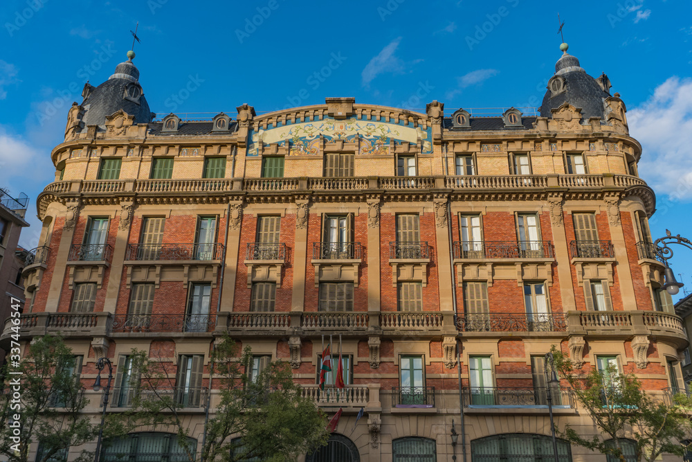 Old library building in Pamplona in Navarra, Spain, located in Plaza San Francisco, with a red brick facade with a blue mosaic in the center, two blue tile domes on the sides stone balconies and trees