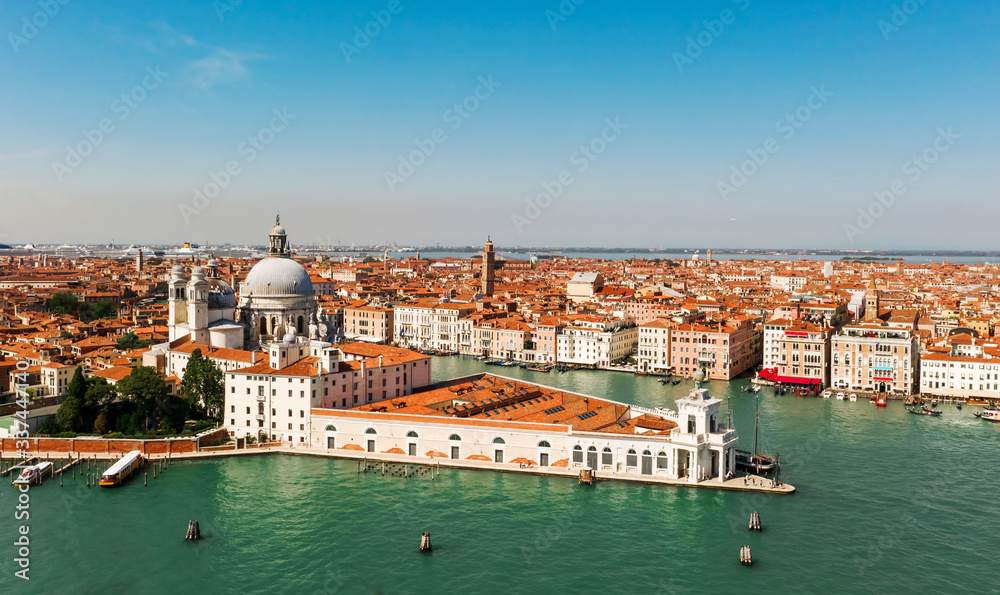 Aerial shot of Venice city and Grand Canal, Italy. View from above. Tiled roofs and nerros streets. Venetian atmosphere. Blue sky and lagoon water. Historical buildings.