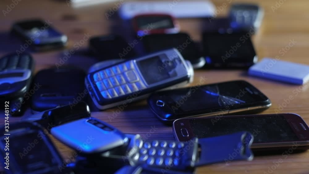 Analog communication. Old broken dusty cell phones lie on table in neon light. Analog communication. Old broken dusty cell phones lie on table in neon light.
