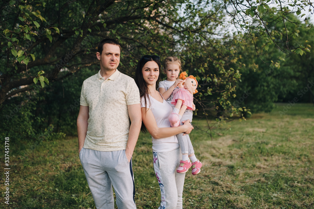 Portrait of a happy family in nature. A guy, a girl and a little daughter are hugging, standing in tracksuits in a green flowered garden. Photography, concept. Portrait of a happy family in nature. A guy, a girl and a little daughter are hugging, standing in tracksuits in a green flowered garden. Photography, concept.