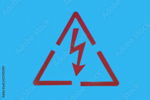 close up photography of a red painted electricity warning sign on a blue metal background