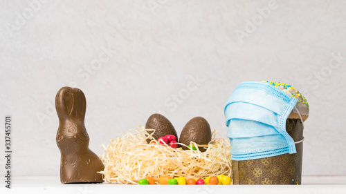 Easter cake in protective medical face mask and chocolate eggs and rabbit, close-up. Protection against viruses.